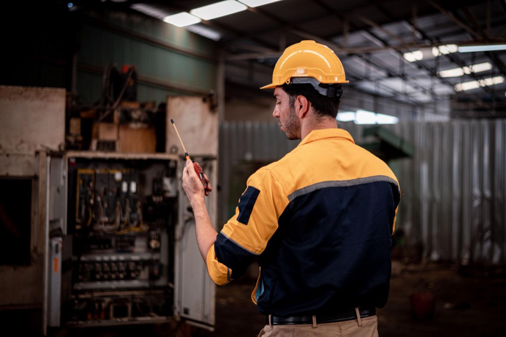 Técnico com capacete e EPI em painel elétrico industrial